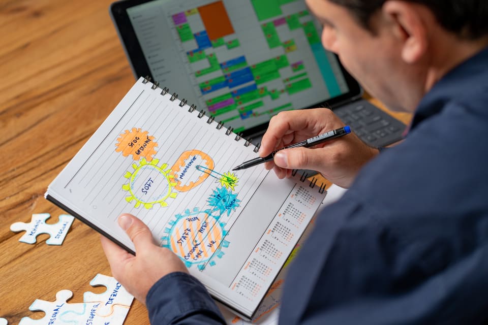 Alex Onețiu desenează pe un caiet schema unui sistem, cu un calendar deschis pe laptop